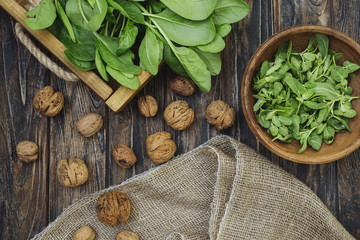 Rustic wooden tray with fresh organic local spinach leaves plants on a table. Clay plate with greens, walnuts in shells. Vegetarian vegan healthy food. Grow your own, eat local produce