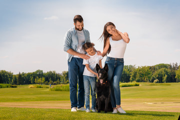 Naklejka na ściany i meble Happy multiethnic family standing with dog on green lawn