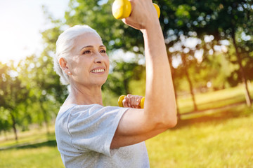 Cheerful smiling aged woman doing sport exercises in the park