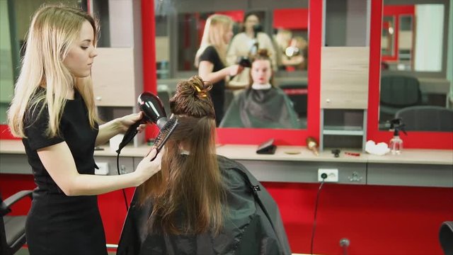 A woman who is a hairdresser, combs her hair for a beauty salon client with a hairdryer and a comb, the messenger came to get a new hairstyle and change the immige