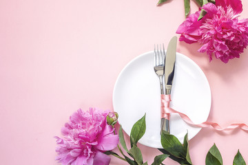 Festive table setting with cutlery and pink peonies  on pink table. Copy space.