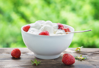 Yogurt with strawberries in a white bowl on a wooden table in the garden. Focus concept.