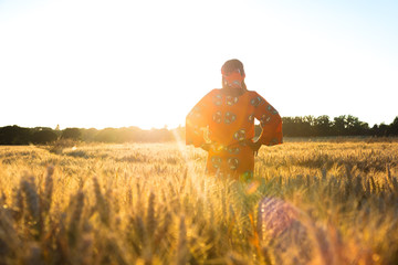 African woman in traditional clothes standing in a field of crops at sunset or sunrise