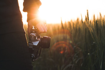 The woman with a retro camera against the background of a sunset in the wheat field