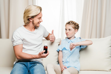 Smiling father holding medicine and showing thumb up while daughter showing thumb down