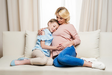 Happy pregnant woman with cute little daughter hugging at home