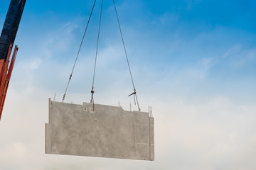 Construction site crane is lifting a precast concrete wall panel.