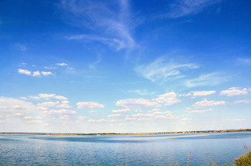 Summer blue sky with cumulus clouds over water.