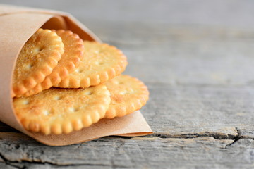 Dry wheat cookies in a wrapping paper and an old wooden table. Vegan salty crackers snack idea for kids or adults. Rustic stile. Closeup