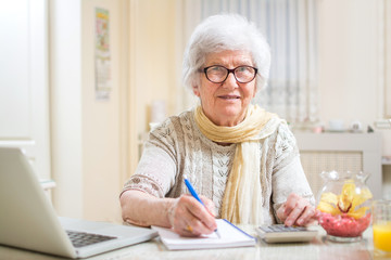 Senior woman with papers and calculator doing financial calculation at home.