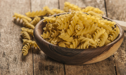 Pasta fusilli in a wooden bowl on wood background for healthy recipes.