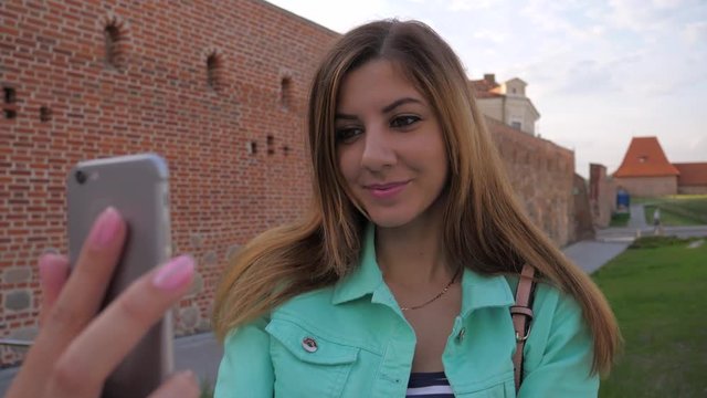 Brunette girl uses a smartphone and taking a selfie on a beautiful background.
