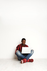Smiling black man using laptop sitting on the studio floor