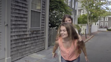 Carefree Teen Girls Walk Down New England Neighborhood Street, Girl Gives Friend A Piggyback Ride, They Smile/Laugh
