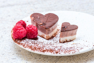 Valentines day desserts. Heart shaped chocolate cake slices on white plates with raspberry fruit decorations. Bright table.