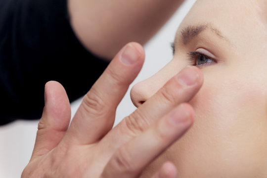 Fingers applying makeup foundation under girl eyes