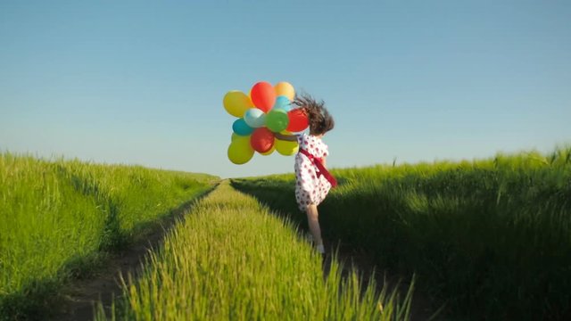 Child with balloons in the field. Happy child runs in a wheat field with balloons.