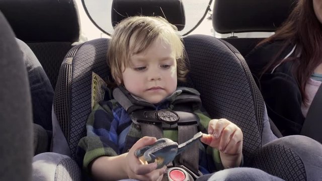 Little Boy Plays Quietly With His Toy Dinosaur In His Car seat