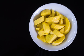Slices of mango fruit in white plate on black background top view with copy space