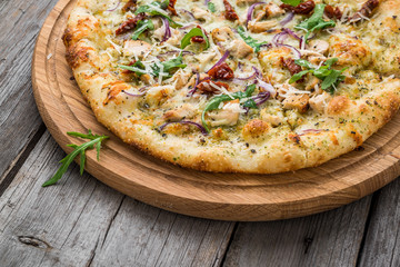 pizza with sun-dried tomatoes, prosciutto, arugula and parmesan cheese on a plate on the table