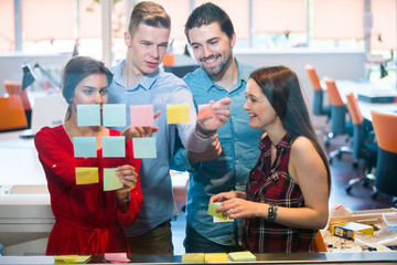 business, startup, planning, management and people concept - happy creative team with stickers on office glass board talking at office