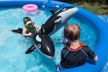 two boys in swimming pool with lots of toys having water gun fight