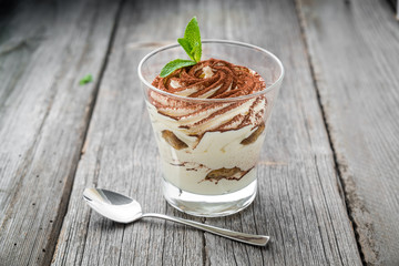 Traditional Italian dessert tiramisu in a glass. On a wooden table
