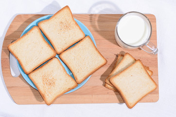 Square toast on a blue plate on a wooden board and a mug of milk