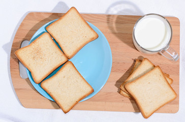 Square toast on a blue plate on a wooden board and a mug of milk