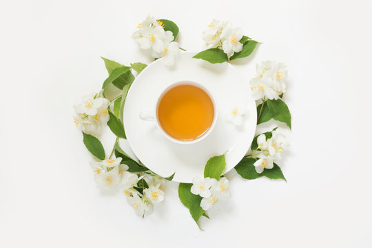 Jasmine flowers around cup of green tea on white background. Top view and concept.