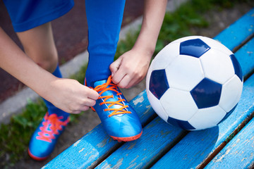 Boy football soccer tying laces of boots on bench