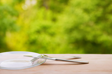 Plate, fork and knife on wooden table outdoors