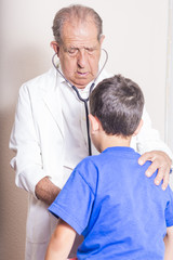 Obraz premium Senior male doctor with stethoscope examining a young boy child