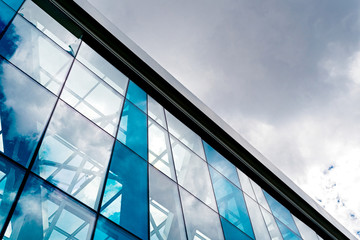 Bottom view of modern glass blue business centre architecture, free space. Sunlight reflection on glass abstract building. Sky with clouds background. Windowed corner of office building