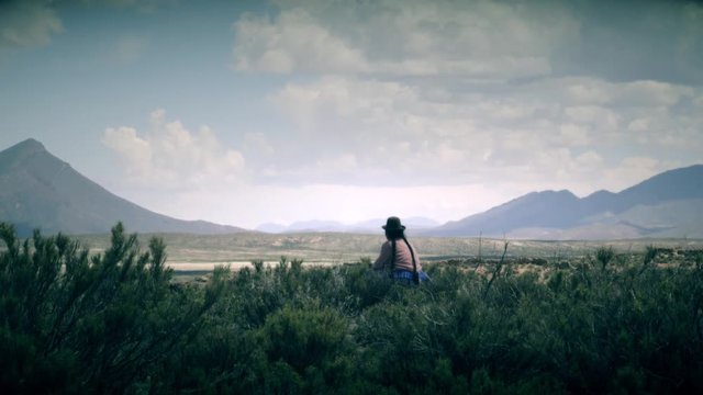 Indigenous woman seated on the bolivian fields wearing a traditional bolivian hat. 4k