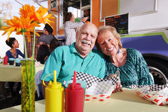 Smiling Elderly Couple Eating Out From A Food Truck