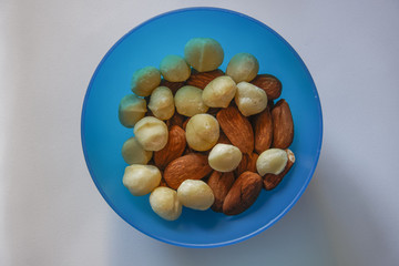 Macadamia and almonds mixed roasted nuts top closeup view.
Collection of healthy nuts served on a blue plastic bowl.