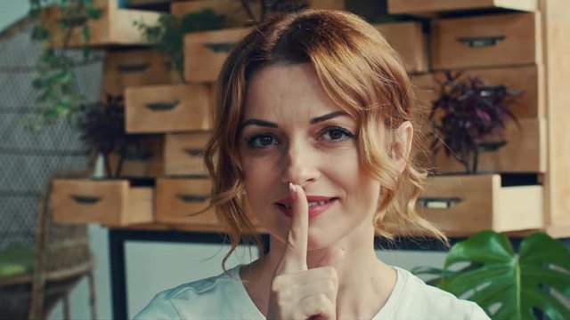 Beautiful adult woman doing silence sign, tss gesture. Happy, smiling model. Indoor, close up view