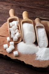 scoop with white sand and lump sugar on brown wooden background