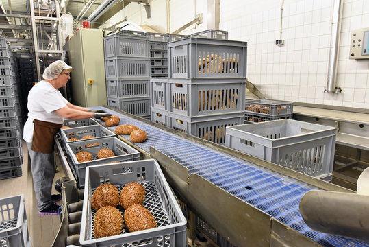 Frau in der Lebensmittelindustrie arbeitet am Fliessband mit Broten in einer Großbäckerei // Woman in the food industry is working  in a large bakery