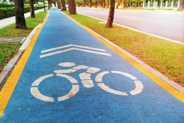 Blue bicycle lane with white cycling sign along side the normal road in city, with a bit sunflare in picture.
