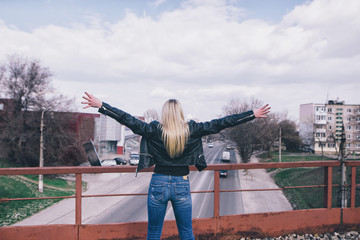 Young woman spreading hands wide open with city on background. Freedom concept. Love and emotions, woman happiness. Toned image