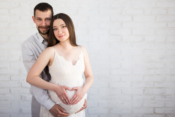 pregnancy and parenthood concept - portrait of beautiful pregnant couple posing over white wall