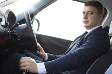 Businessman sitting in his car. Looking at the camera while in traffic. Suit and tie businessman sitting in his automobile.