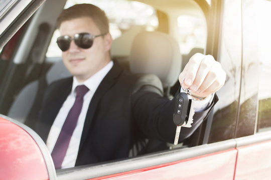 Close-up of a young business man holding car keys. Brand new car. Man smiling while holding car keys. Focus on car keys.