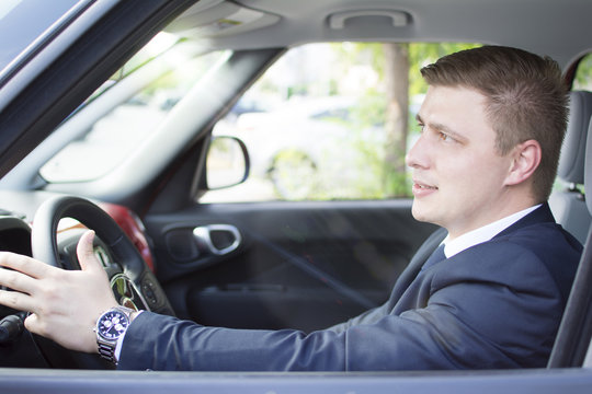 Young and well-dressed businessman sitting in his car. Suit and tie businessman driving his car. Lens flare in background.
