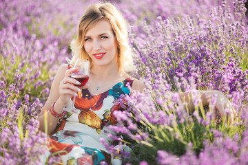 Beautiful blonde sexy woman is drinking red dry wine in lavender field