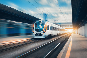 High speed train at the railway station at sunset in Europe. Modern intercity train on railway platform. Urban scene with beautiful passenger train on railroad and buildings. Railway landscape