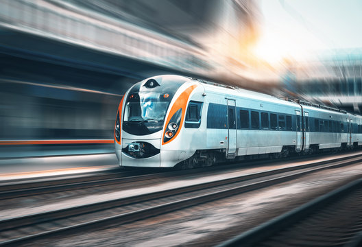 Fototapeta High speed train in motion at the railway station at sunset in Europe. Modern intercity train on the railway platform with motion blur effect. Industrial landscape with passenger train on railroad