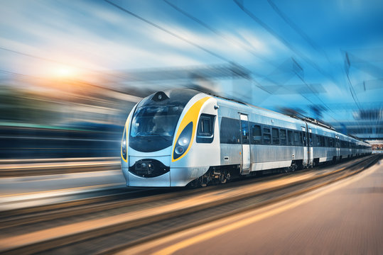 Fototapeta High speed train in motion at the railway station at sunset in Europe. Modern intercity train on the railway platform with motion blur effect. Industrial landscape with passenger train on railroad